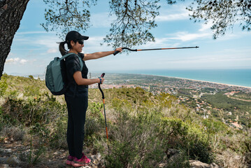 Woman points her hiking stick at the Mediterranean coast.