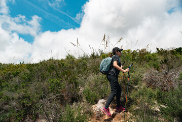 Woman hiker walking on a scenic mountain trail under a blue sky with clouds.