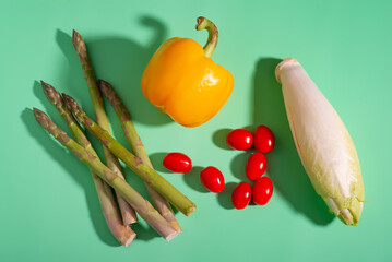 Fresh asparagus, peppers, and tomatoes displayed on a vibrant green surface