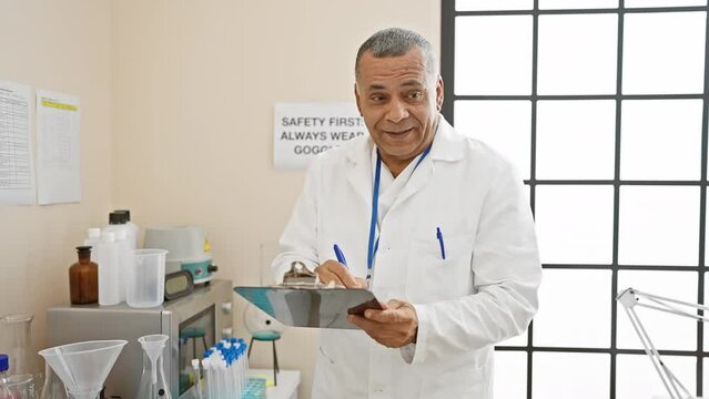 Hispanic scientist working in a laboratory, with man, clipboard, lab, professional, equipment, mature, chemistry, medical, research, technician accurately summarizing the scene.