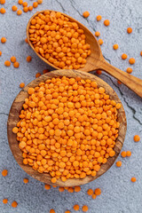 Photo of red lentils in wooden bowl with wooden measuring cup on wooden background.  Healthy...