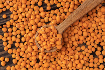 Photo of red lentils in wooden bowl with wooden measuring cup on wooden background.  Healthy...