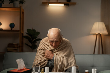 Unhealthy man sitting covered with blanket, feeling sick, suffering from flu. Unhealthy elderly man...