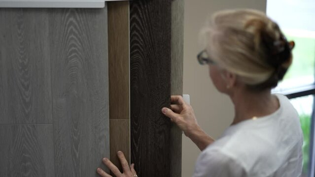 Pretty mature woman looking at display of lvp, luxury vinyl plank wood samples in a floor store for a home remodeling redecorating project.
