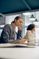 Stylish female manager working on laptop while sitting the desk in office on colleague background