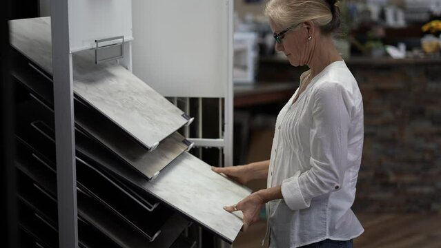 Side view of pretty mature woman running hand across touching luxury vinyl tile samples in a floor store for a home remodeling project.