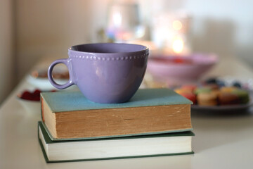 Plate of pastel macarons, cookies and chocolate, cup of tea of coffee, glass of bubble water, various berries, books and accessories on the table. Selective focus, pastel colors.