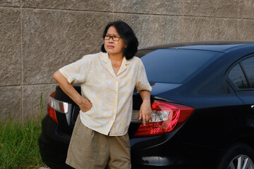 Unhappy expression of a woman leaning on the car trunk, looking bored waiting for someone