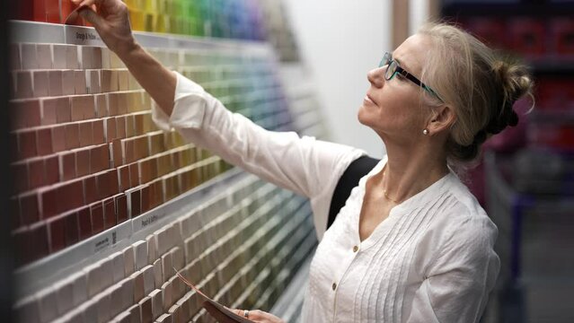 Closeup of smiling mature woman comparing color swatches at a paint display shopping for home redecorating renovation project, in a hardware store.