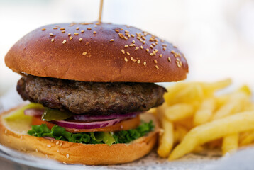 Close up of a hamburger with sesame seeds on the bun. There are golden french fries on the side.