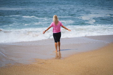 A girl in a pink T-shirt on the Nazare beach near the ocean with waves.