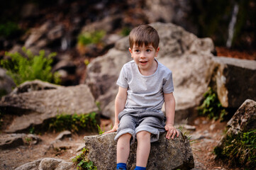 Young boy in a gray t-shirt and denim shorts sitting on a rock, smiling and enjoying the outdoors....