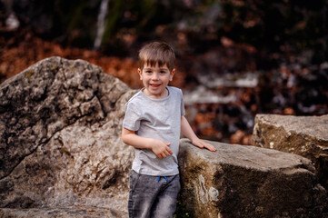 Young boy in a gray t-shirt and denim shorts laughing and playing among large rocks. Capturing a...