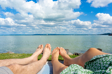 couple hanging out chilling on a blanket next to Lake Balaton in Hungary from Badacsony beach with blue sky and cloud refletion on the water