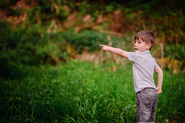 Young boy in a gray t-shirt and jeans, enthusiastically pointing at something in the distance while...
