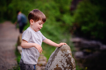 A young boy explores rocks on a nature path, showing curiosity and engagement with his...
