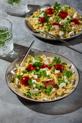 Farfalle pasta with  green peas, tomatoes and soft cheese on gray table. Vegetarian food.