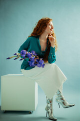 Beautiful fashionable redhead freckled woman with long curly hair, wearing trendy green satin...