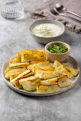 Oven baked zucchini wedges served with green pesto and greek yogurt on gray background. Vegetarian food concept.