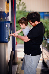 Father holding his young son as they interact with an outdoor payment terminal. The child eagerly inserts a card while the father supports him, demonstrating family bonding and learning.