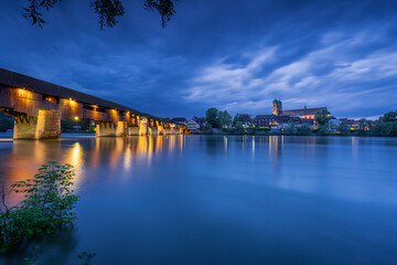 skyline of bad säckingen germany at night with reflection of the illuminated ancient wooden bridge and saint fridolin church in the river rhine 