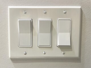 Three large wall mounted toggle light switches and plastic face plate.