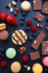Macarons, chocolate, cookies, berries and various nuts on dark blue background. Top view.