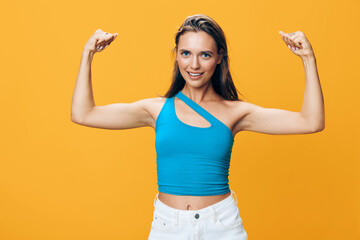 Powerful woman showing strength and confidence in blue top flexing biceps on yellow background
