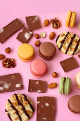 Pastel macarons, almond chocolate, peanut butter cookies and various nuts on bright pink background. Selective focus.