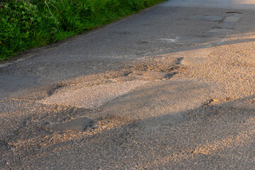A tarmac road with large potholes on a country lane in England, UK