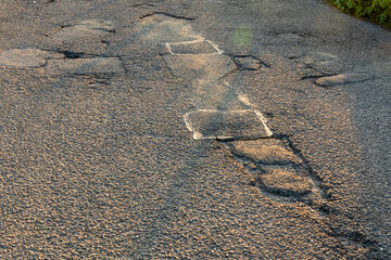 An asphalt or tarmac country road with potholes in need of repair in England, UK