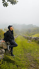 Joven viajero contemplando la naturaleza en un día nublado, con su mochila bajo las nubes blancas,...