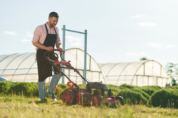 Using lawn mower. Adult farmer is outdoors