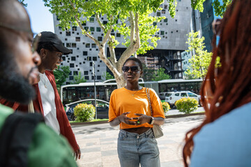 Interested african american young woman in sunglasses standing on street chatting with friends...