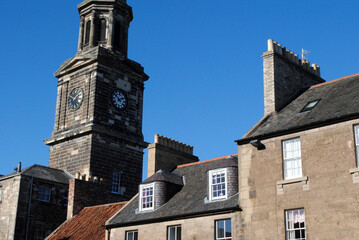 Old Stone Church Tower and Clock seen from Street with Old Buildings and Blue Sky