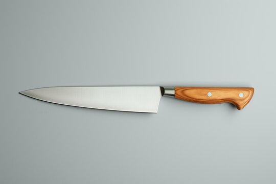 High-quality chef's knife with a polished wood handle and a sharp stainless steel blade, isolated on a grey background, depicting a culinary essential tool for cooking and food preparation