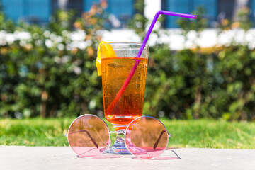 Glass with cocktail with drinking straw and sunglasses outdoors.