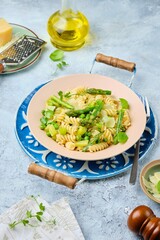 Pasta primavera, fusilli with green peas, asparagus and parmesan cheese in a ceramic plate on a gray concrete background. Asparagus recipes. Italian Cuisine.