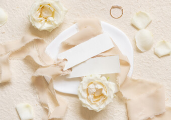 Small horizontal cards near cream roses and petals, ring and silk ribbons top view, wedding mockup