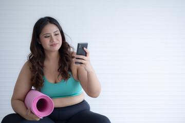 chubby woman sitting use mobile phone and holding mat yoga	
