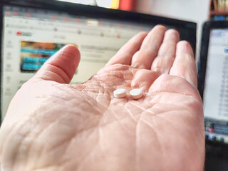 Close-up of an adult hand holding two small white pills. Close-Up of Two Pills in an Open Palm Indoors