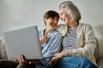 Two older women sitting on a couch, engaged with a laptop.