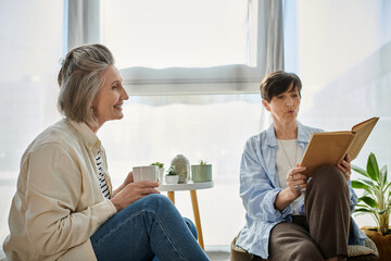 Two women, immersed in a book, sit together in a chair.