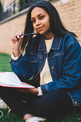 Attractive afro american student in trendy denim jacket doing homework sitting outdoors in university campus concentrated on task.Pensive international student preparing for examinations and tests