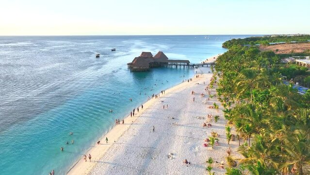 Aerial view of beautiful bungalow in Indian ocean at sunset in summer. Restaurant on the sea. Top drone view of wooden hotel, palm trees, azure water, white sandy beach. Travel in Kendwa, Zanzibar