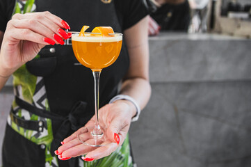 Close-up of a hand holding an orange cocktail garnished with an orange slice