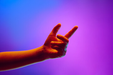 Child showing signs with hand, gesturing against gradient blue purple background in neon light....
