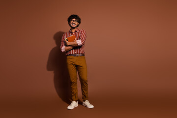 Full body portrait of nice young man hold book empty space wear striped shirt isolated on brown color background