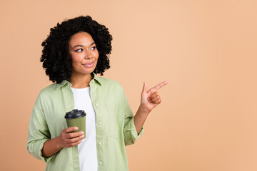 Photo of nice young lady coffee point finger empty space wear green shirt isolated on beige color...