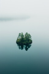 Fototapeta premium Aerial view of a lone island in the middle of a calm lake, surrounded by still water. Highlight the isolation and minimalist beauty of the scene, with the island as the focal point. 